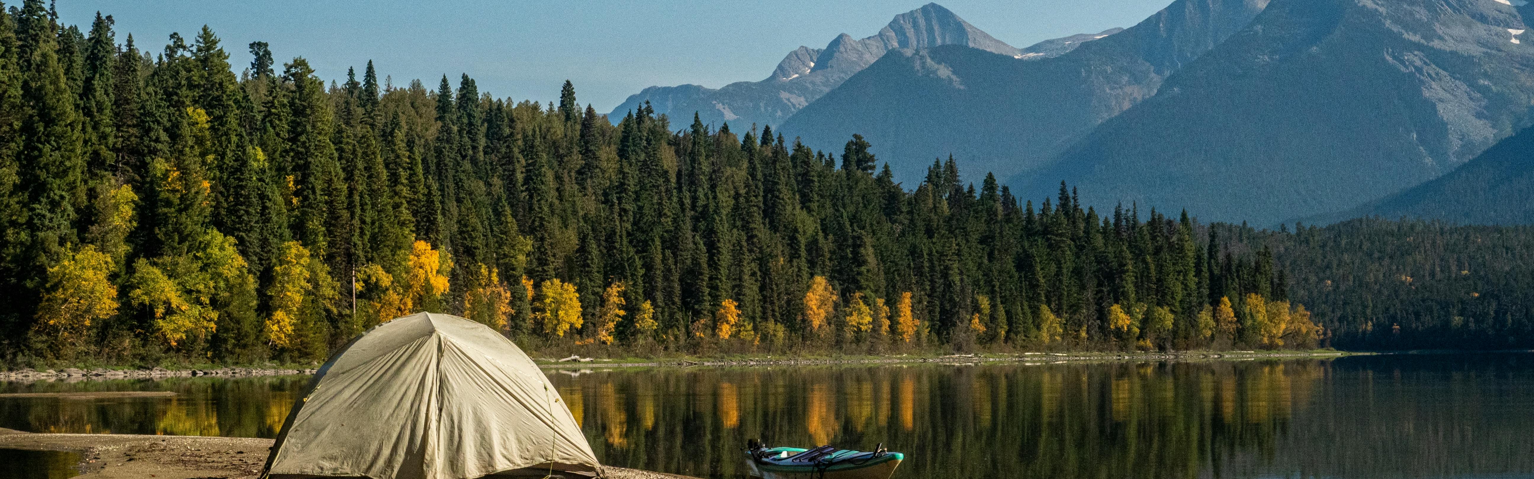A tent is right on the banks of a lake that is overlooked by huge peaks.