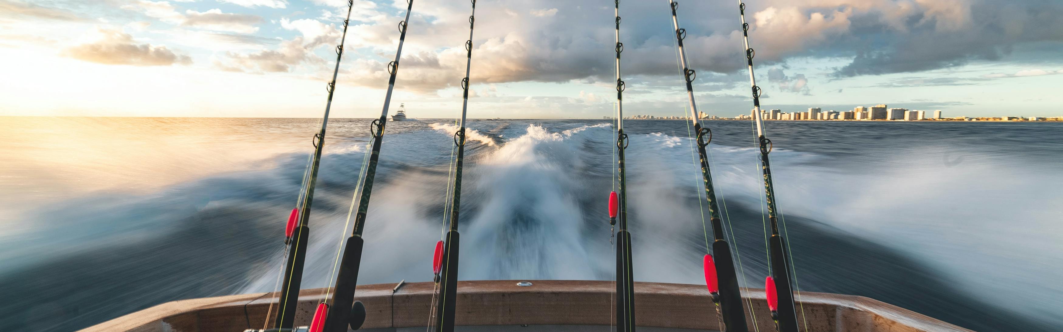 Six fishing rods rest against the back of a boat as it speeds through the water. 