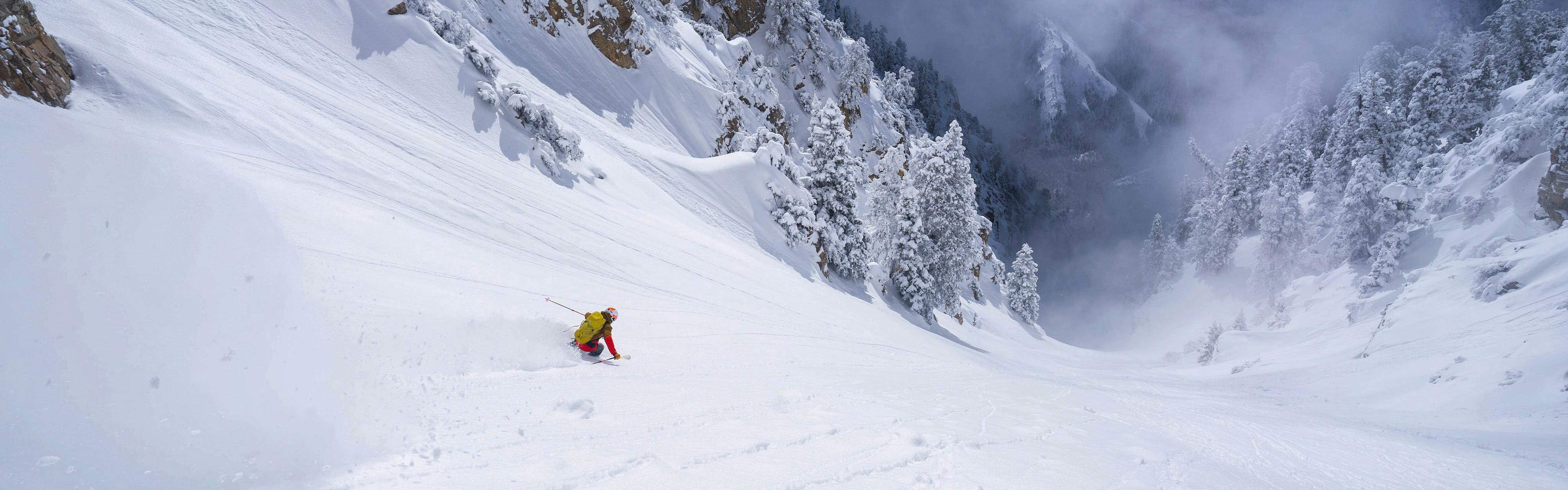 A skier skis down a wide open mountain face with a lot of snow.