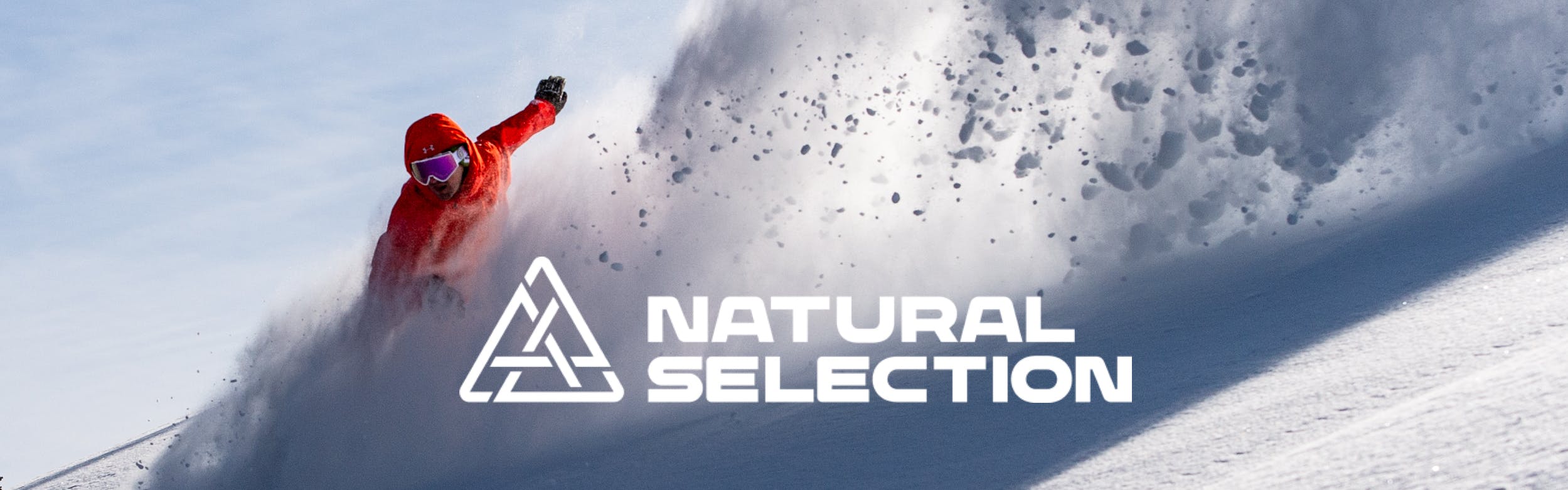 Someone rides downhill setting off a spray of powder. The Natural Selection logo is added on top of the image in white. 