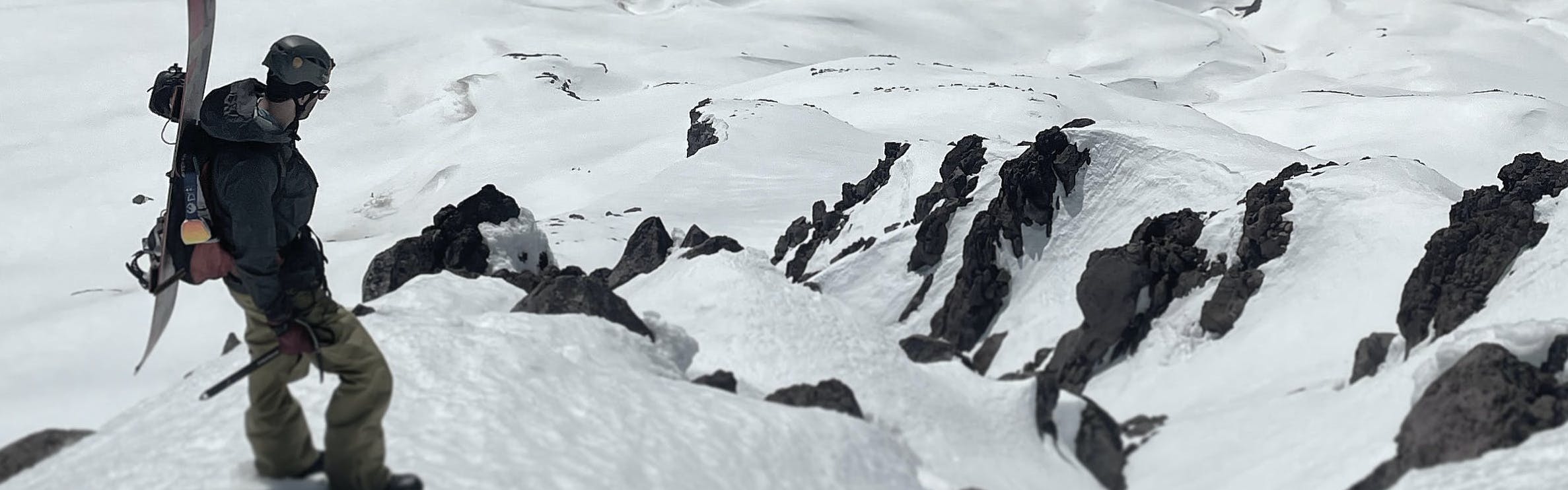 A snowboarder standing at the top of a snowy cliff.