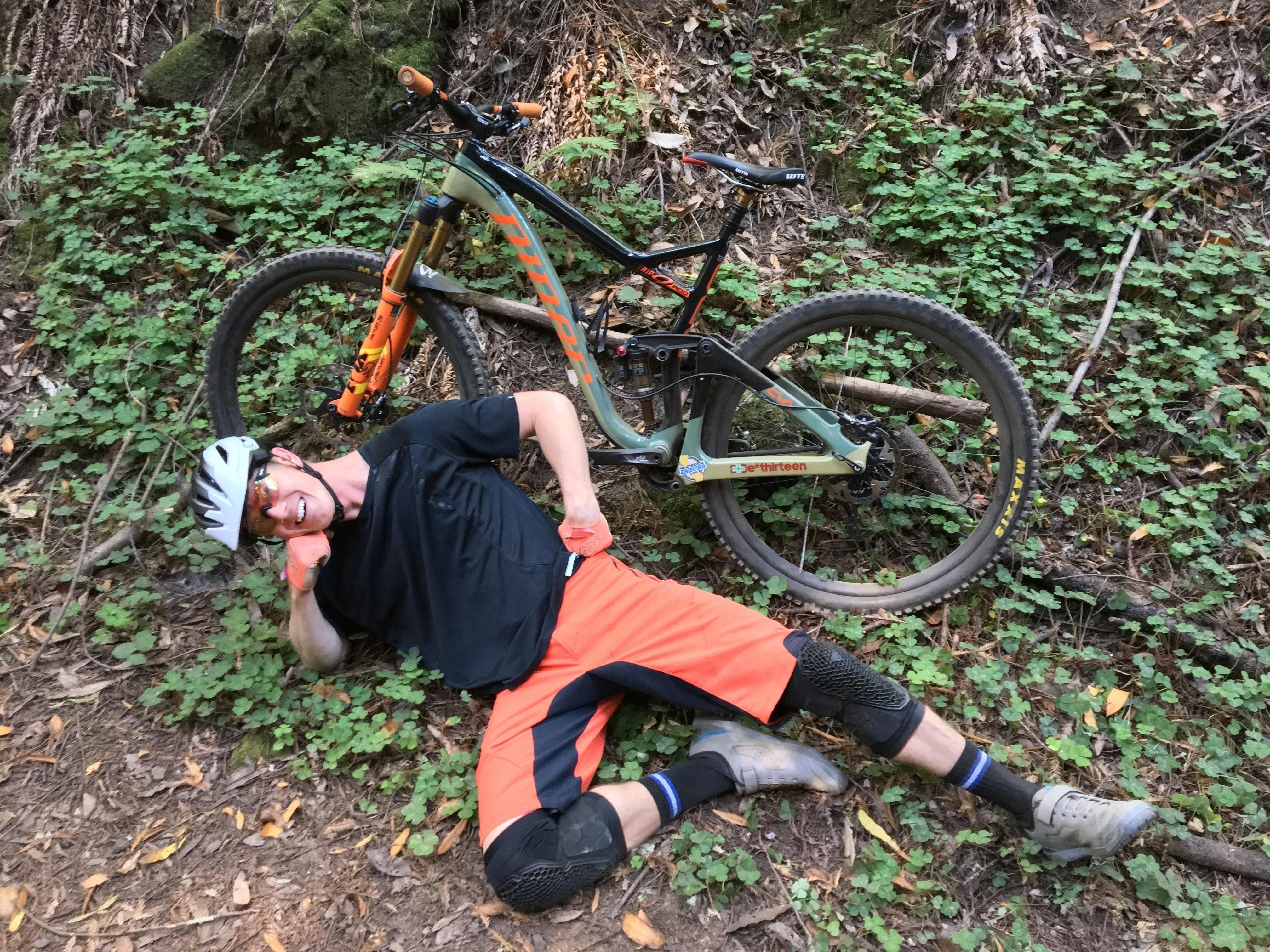 Curated expert Mitch Harnett lounging on the ground in front of his mountain bike in the forest