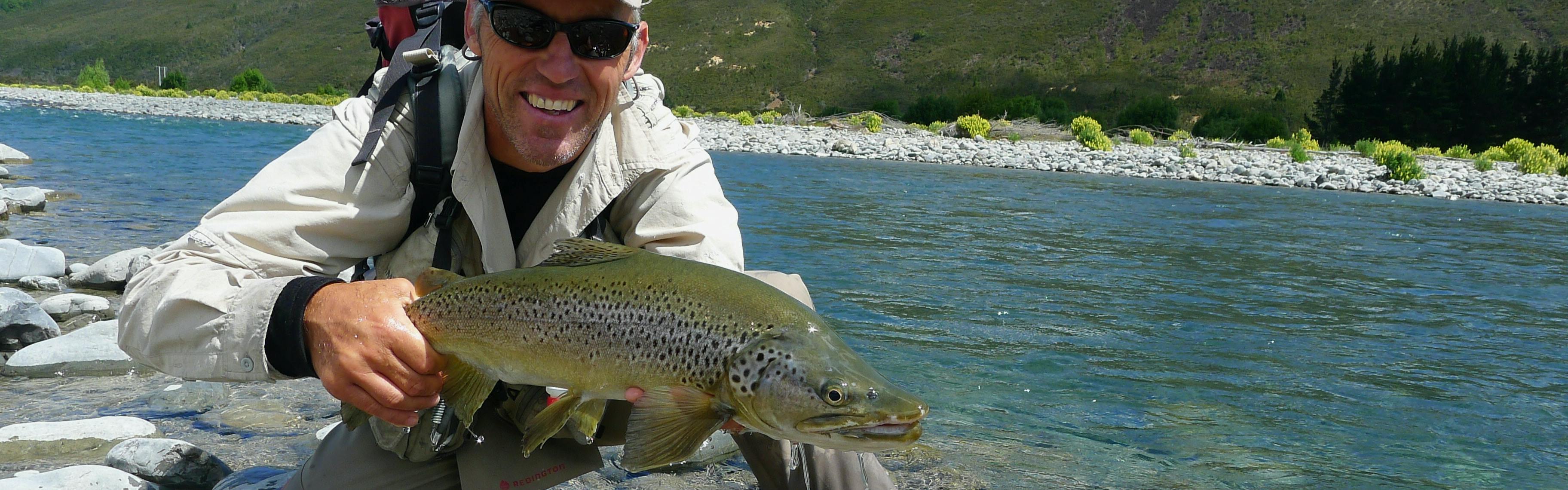 A man holding a trout near a river. 