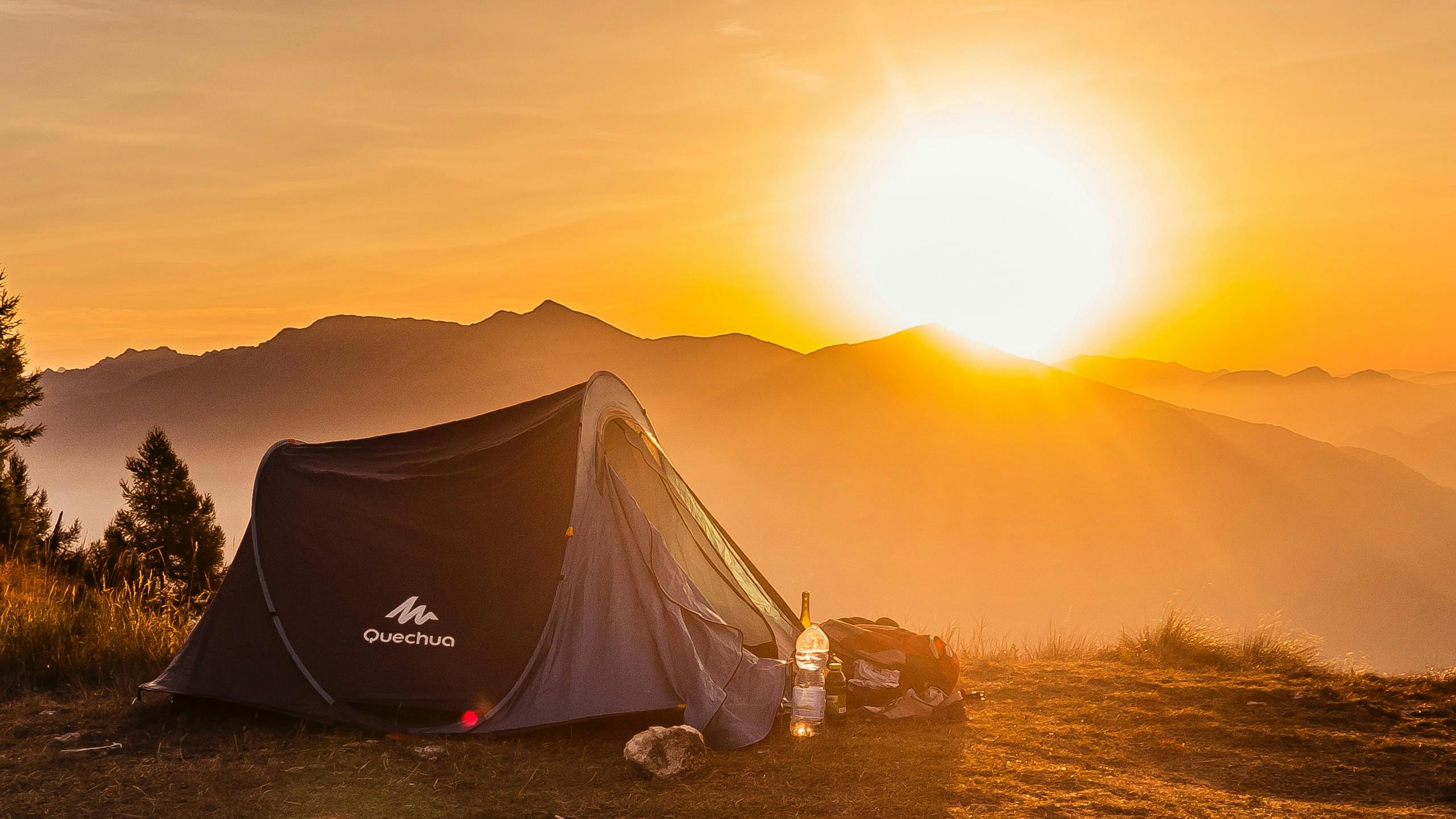 A tent sits on a hill with mountains and a sunset in the background