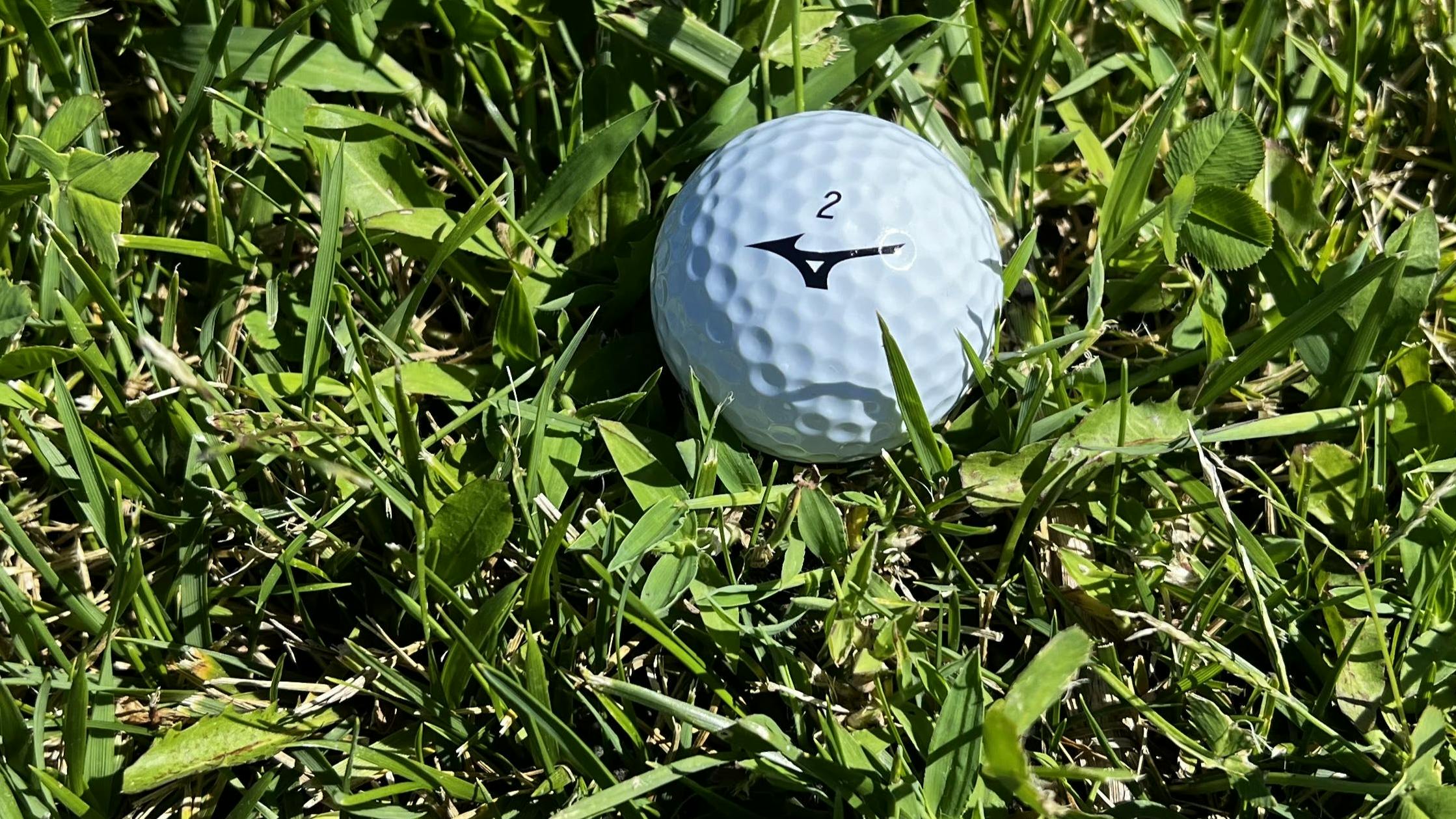 A Mizuno RB Tour X Golf Ball lying in the grass.