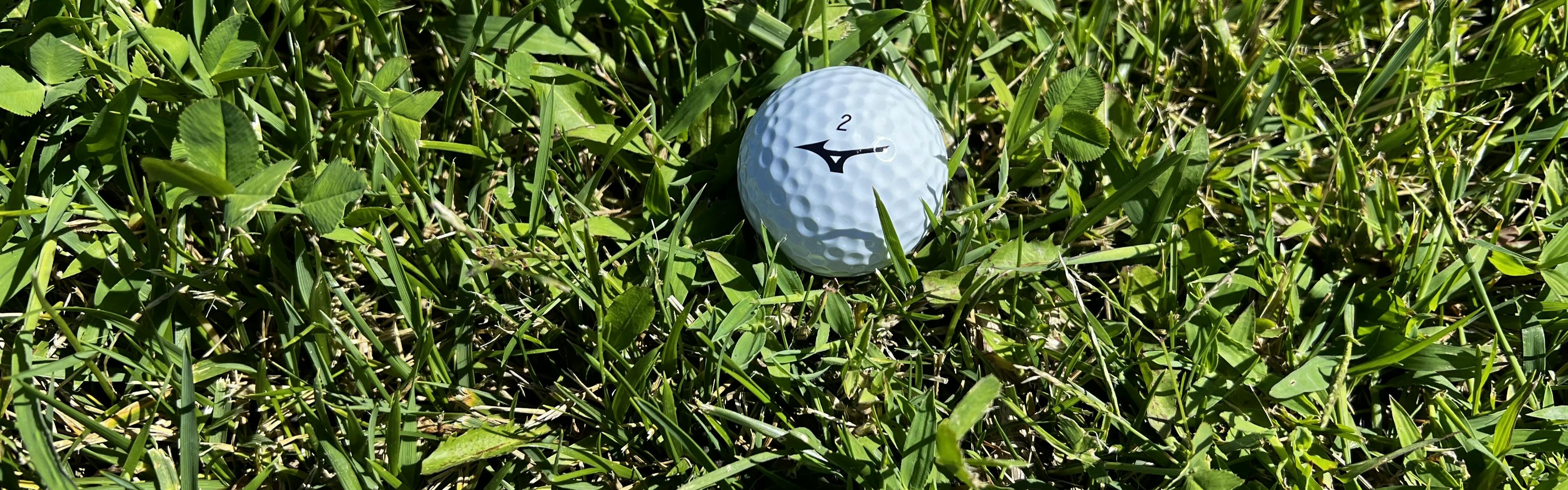 A Mizuno RB Tour X Golf Ball lying in the grass.