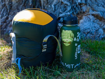 The Nemo Disco 15 Sleeping Bag - Men's packed in its stuff sack sitting next to a Hydroflask water bottle.