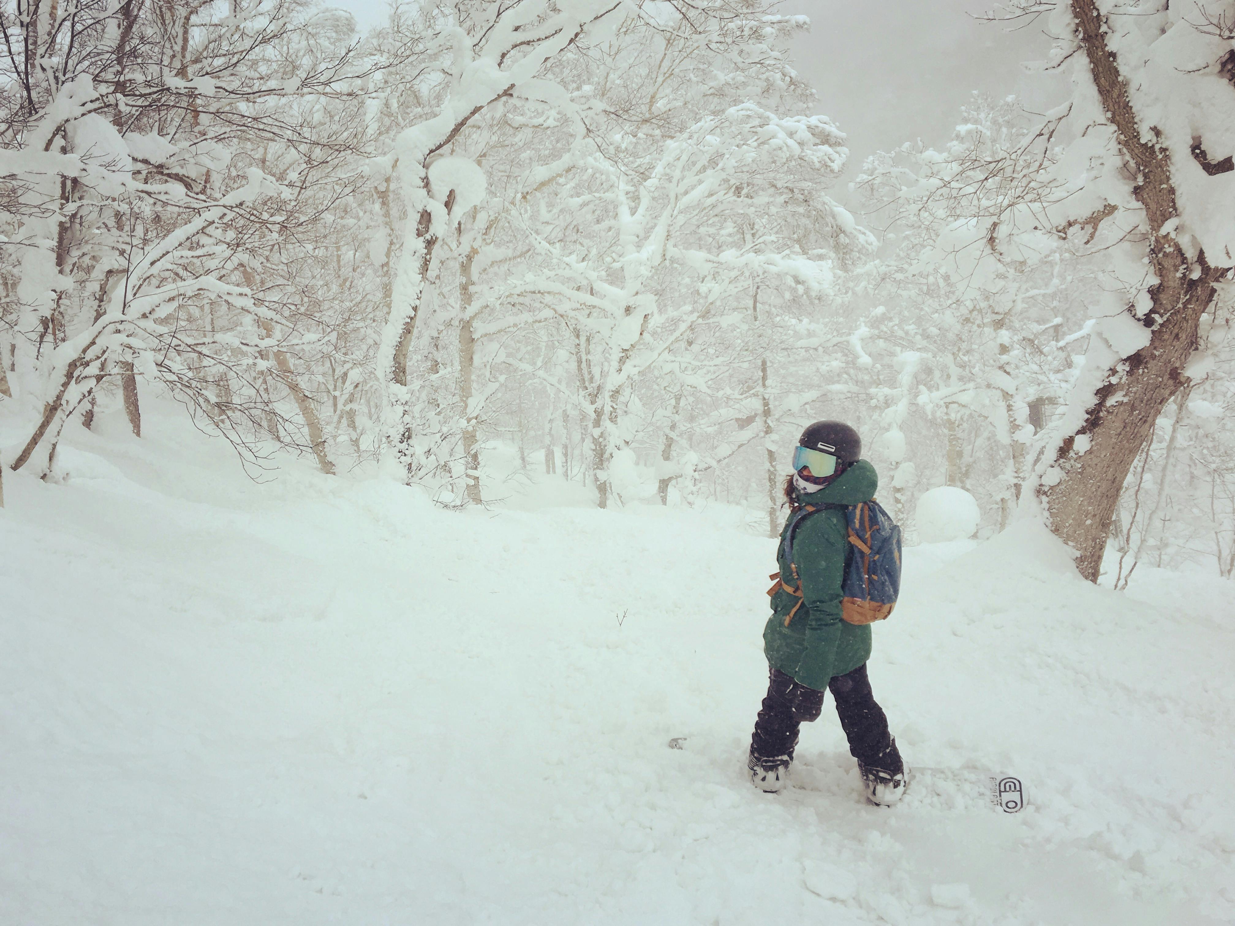 A snowboarder standing in a snowy, wooded area and wearing the Zeal Optics Beacon Goggles · 2021. 