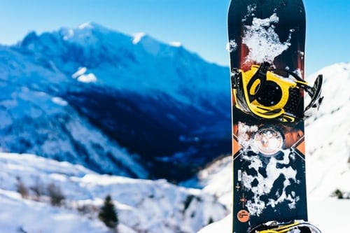 A black and orange snowboard standing in the snow with blue-tinged mountains in the background.
