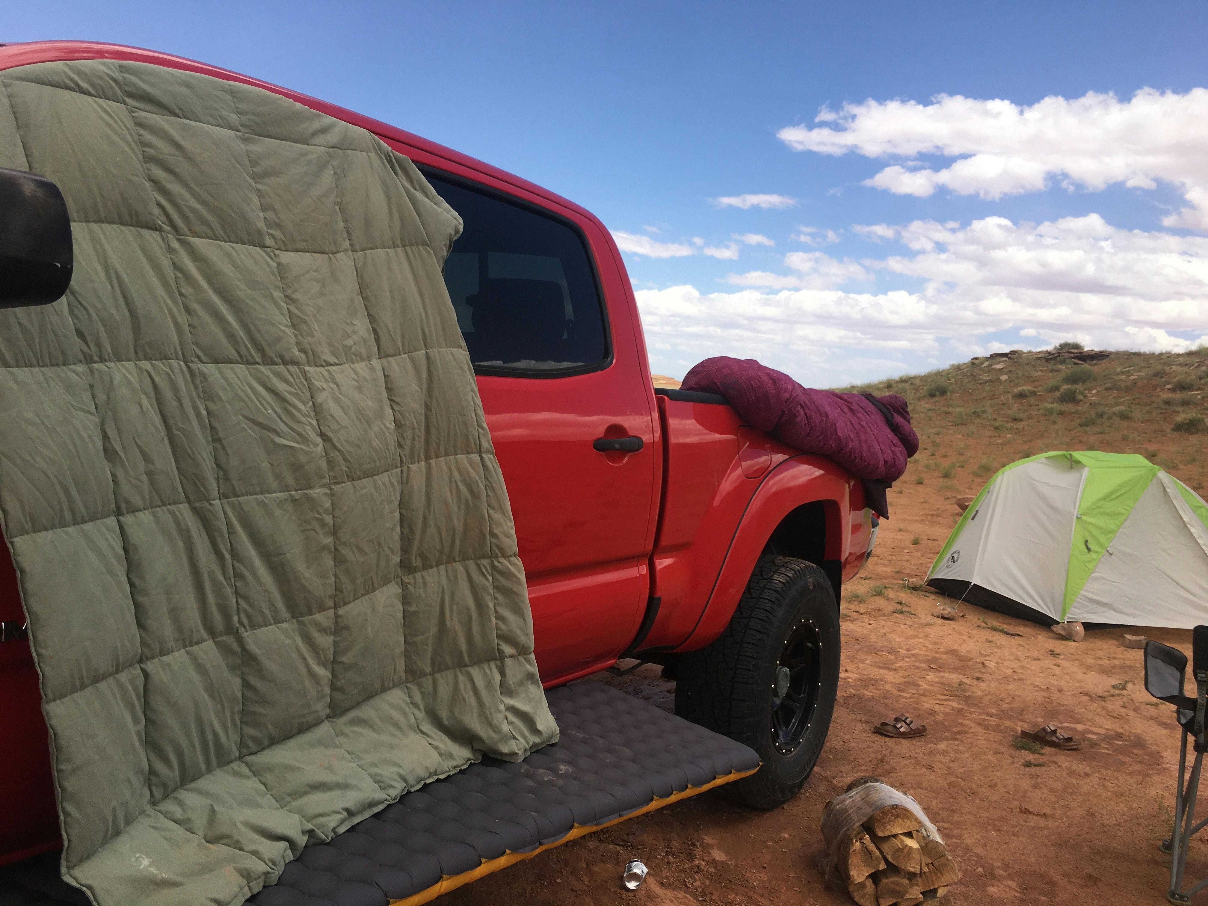 A down blanket is drying on a truck window. There is a tent in the background. 