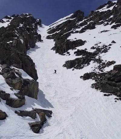 A snowboarder snowboarding down a snowy chute. 