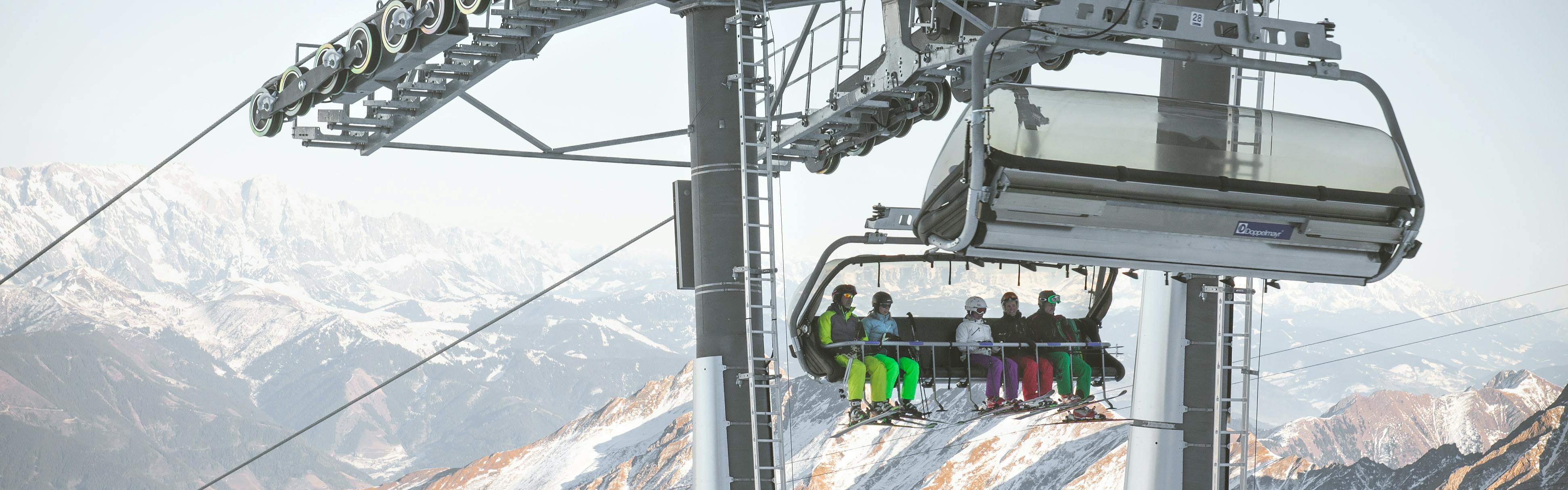 Skiers on a chairlift with snowy mountains in the background. 