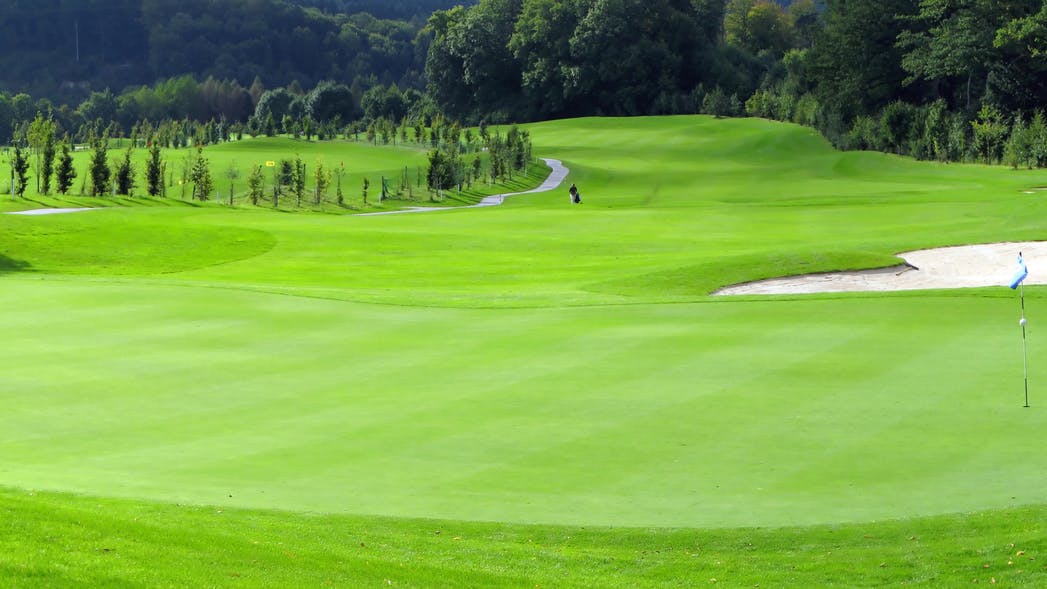 A landscape of a lush, bright green golf course with a sand trap in the distance. 