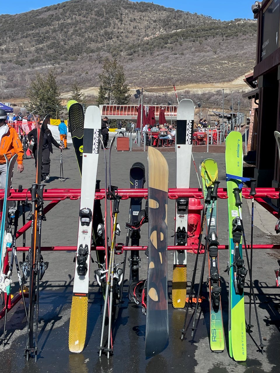Several pairs of skis lined up on a ski rack in a parking lot.