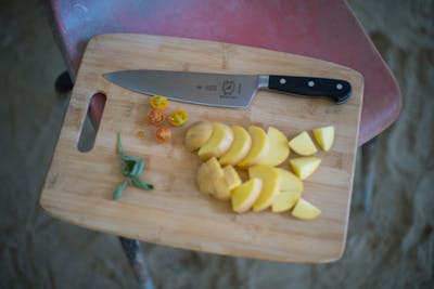 The Mercer Culinary Renaissance Forged Chef's Knife, 8 Inch lying on a cutting board with some potatoes. 