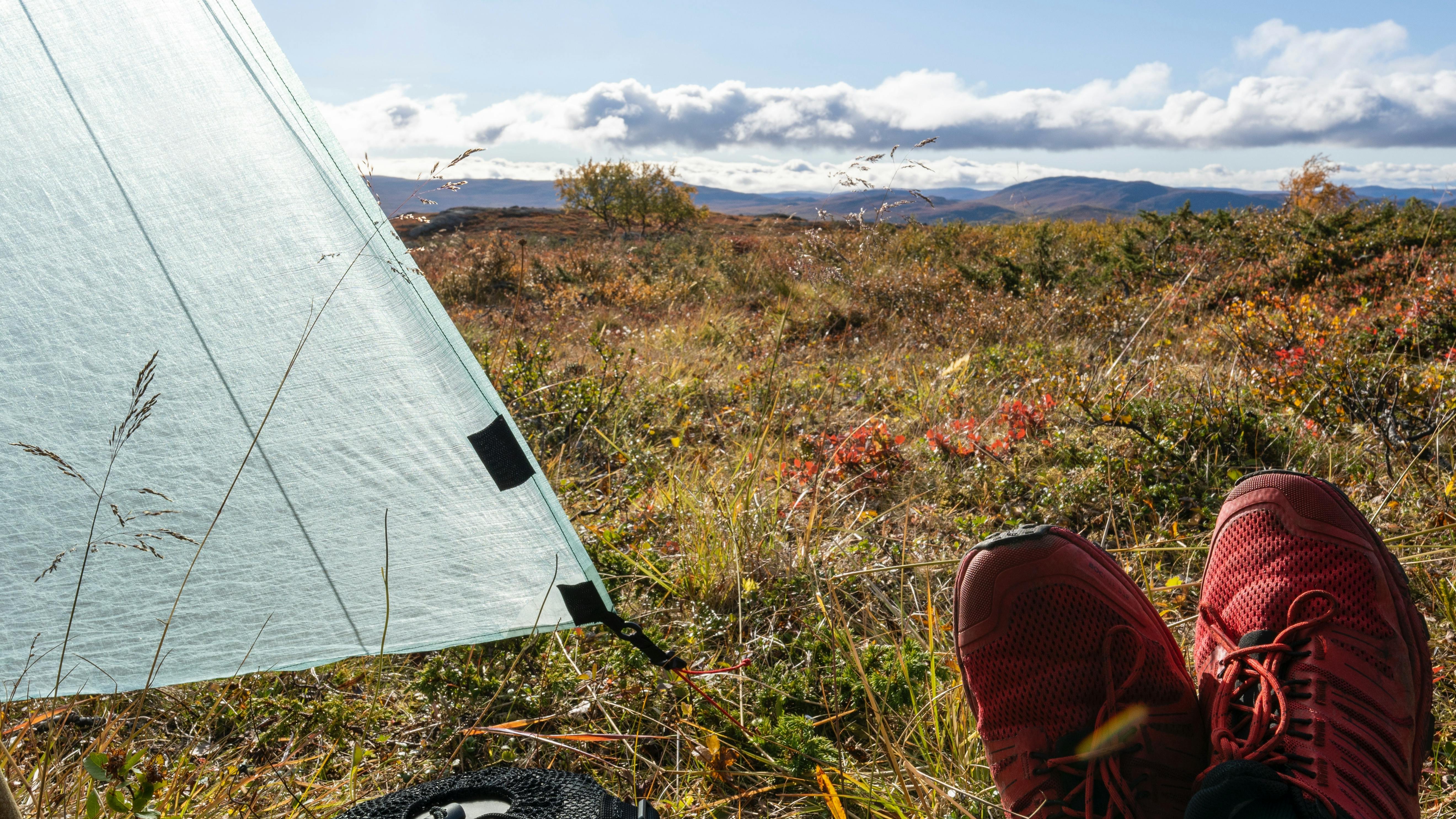 Someone sits next to a backpacking tent that's held up by a hiking pole. 