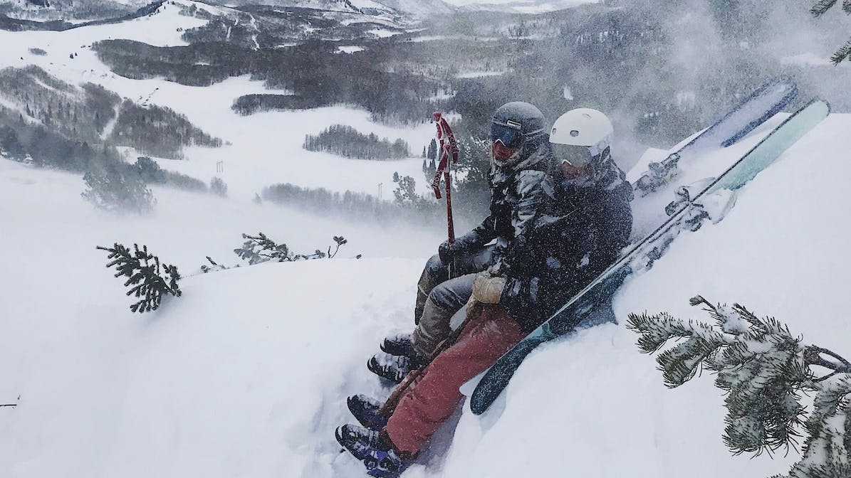 Two skiers sitting in a snowy area next to their skis.