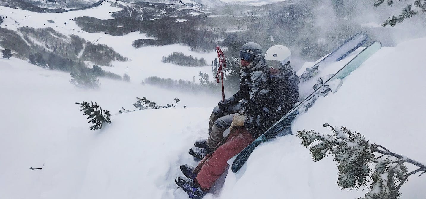 Two skiers sitting in a snowy area next to their skis.