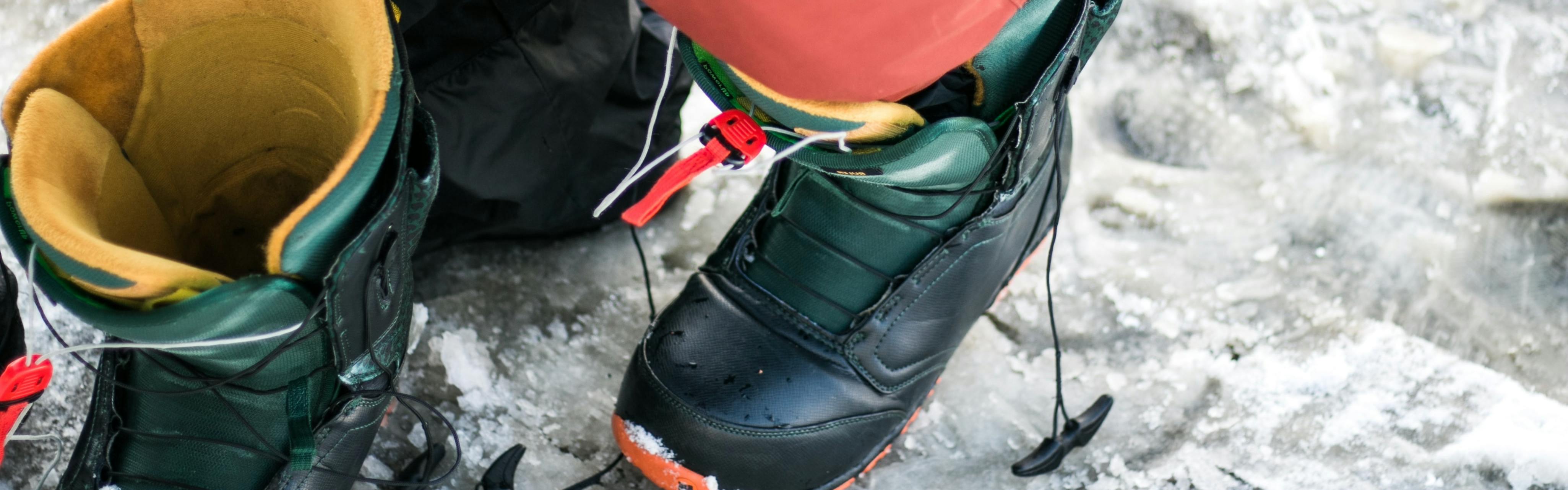 A woman puts her foot in a snowboard boot.