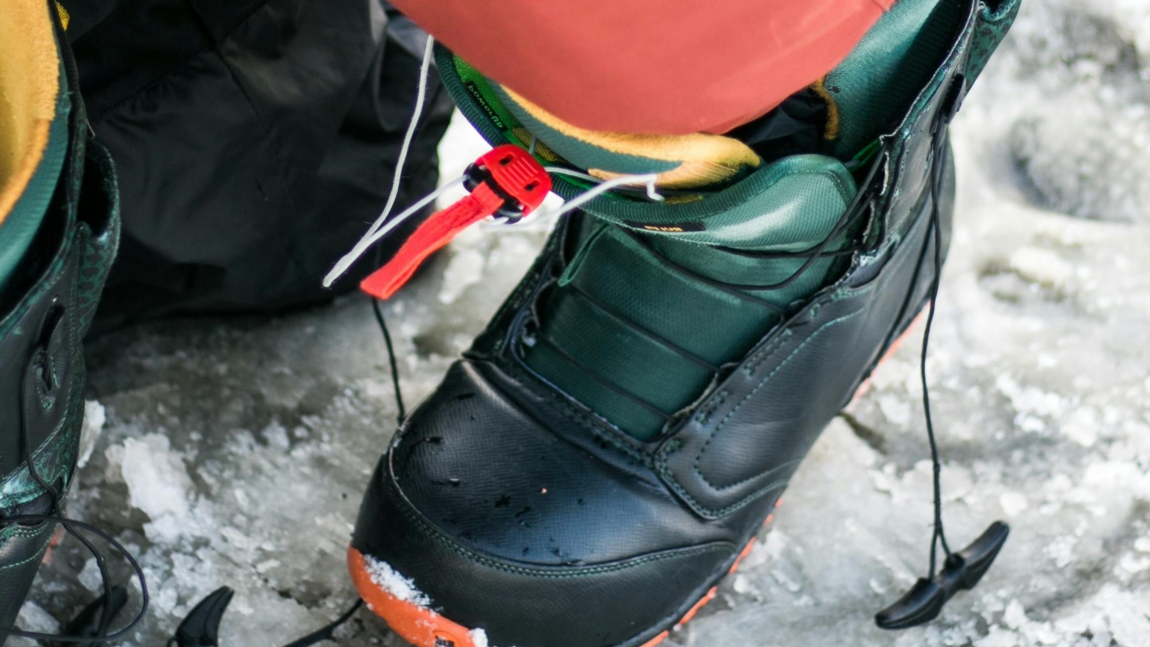 A woman puts her foot in a snowboard boot.