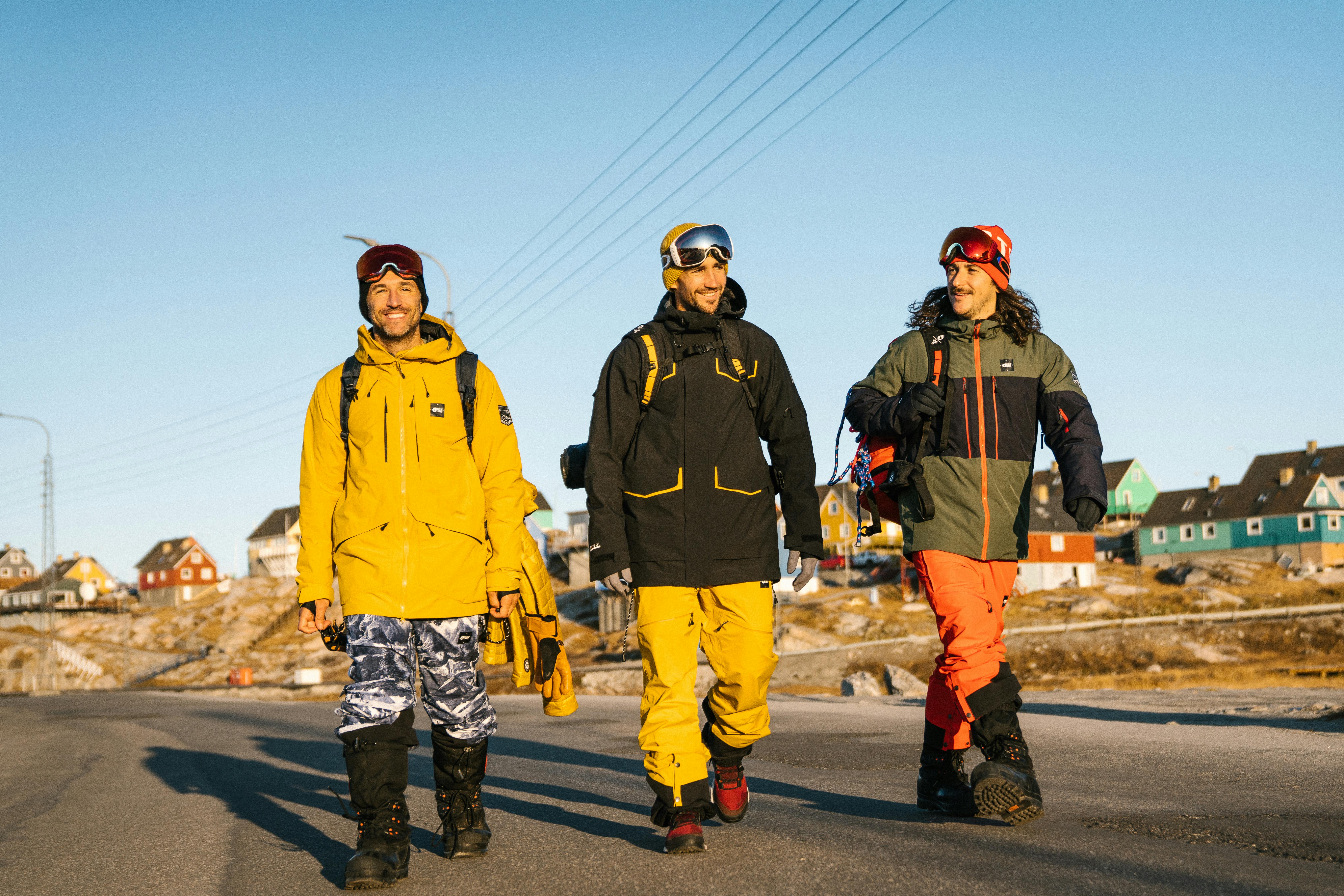Three boarders walking down the street wearing winter sports jackets and pants