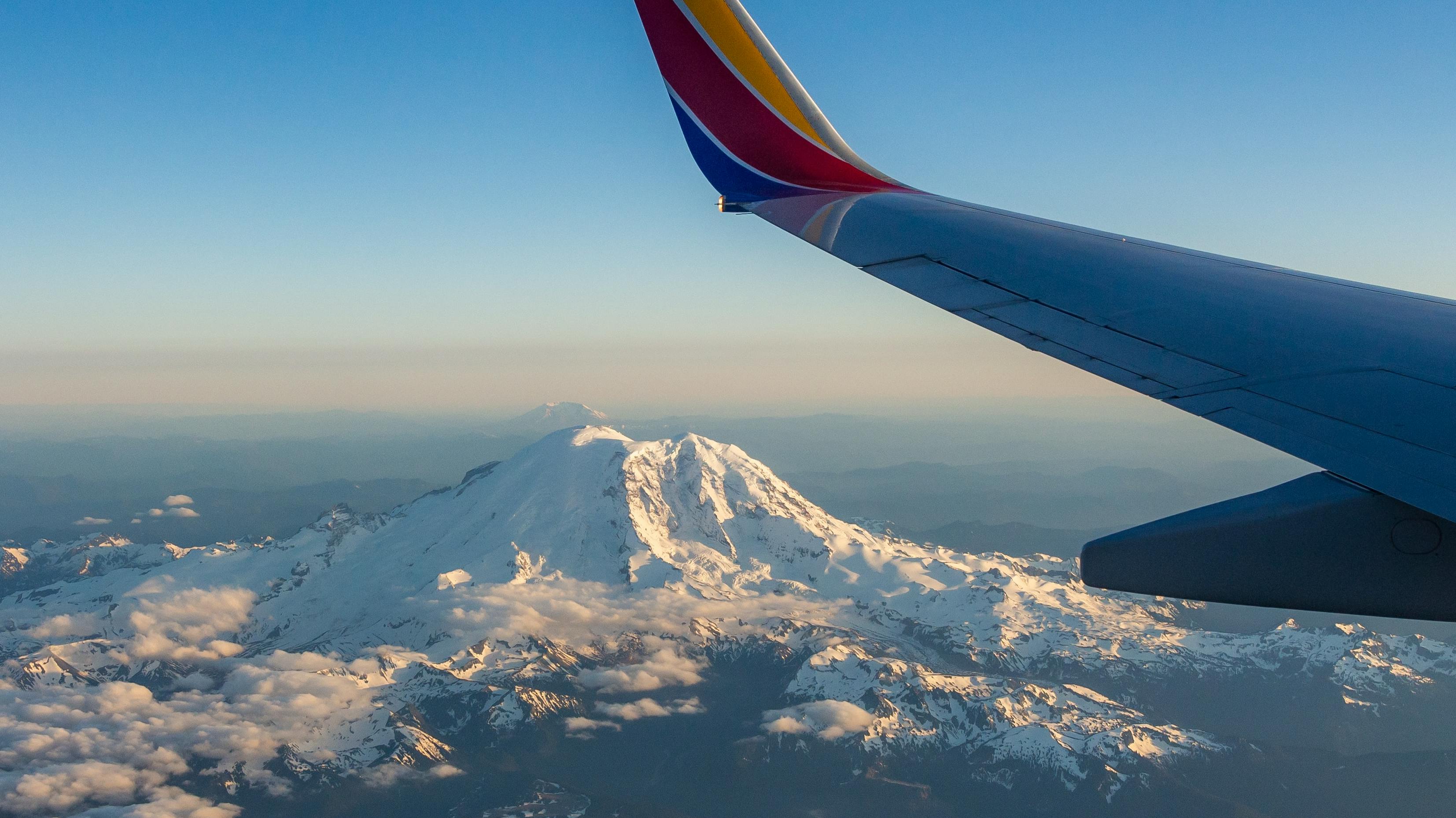 The snowy Mt. Ranier as seen from an airplane with the plane's wing in the view. 