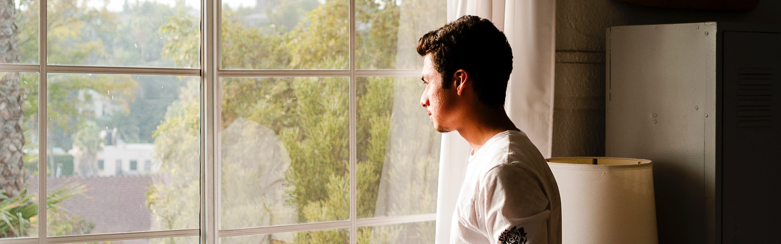 A man looks out a window at home.