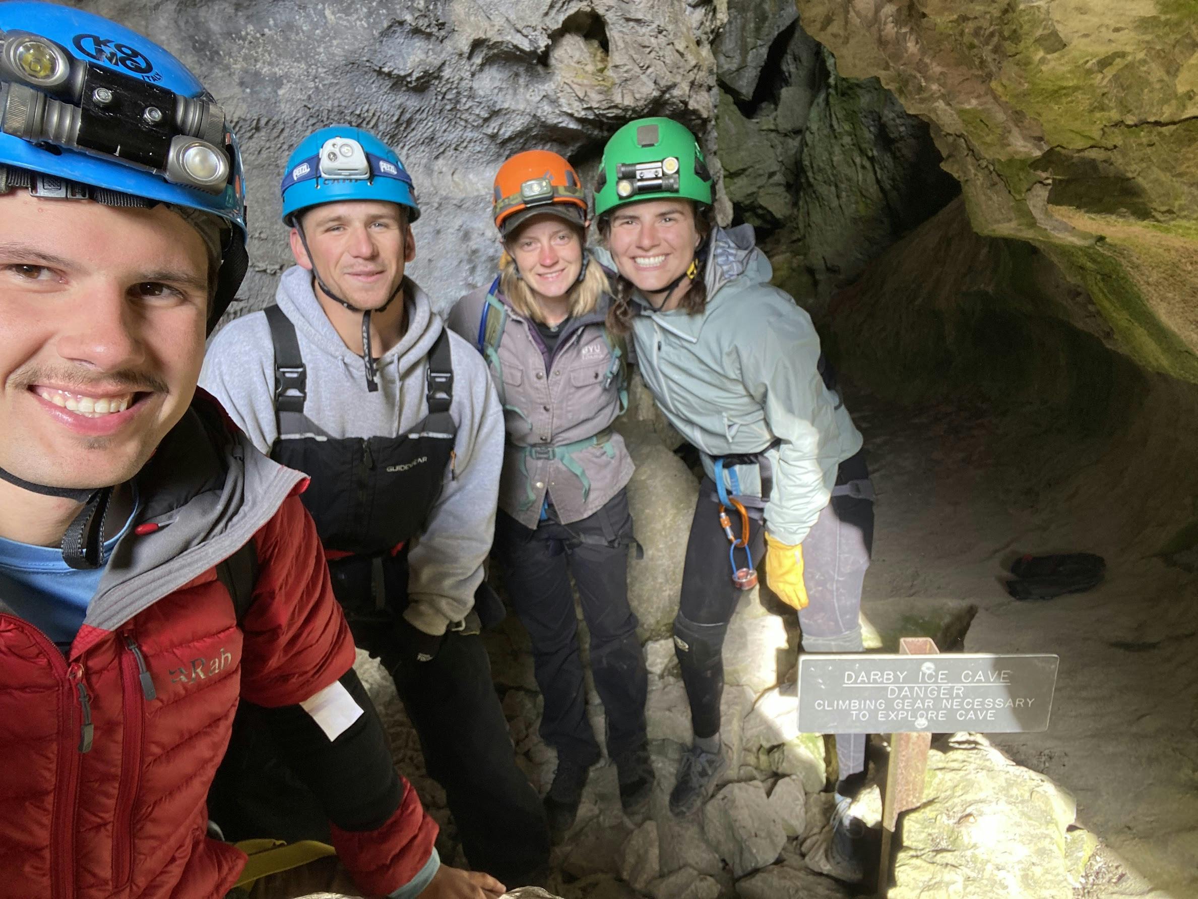 A selfie of four cavers with headlamps and helmets. 