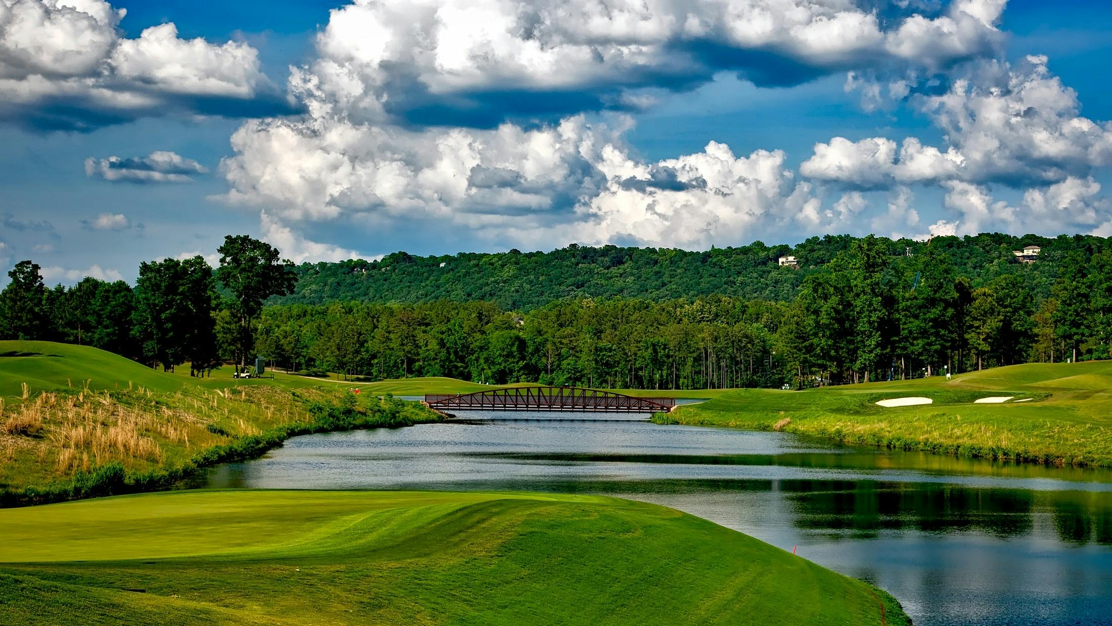 A landscape image of a beautiful golf course with a wooden bridge crossing its water feature. 