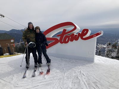 Two skiers standing by a sign at a ski resort that says "Stowe".