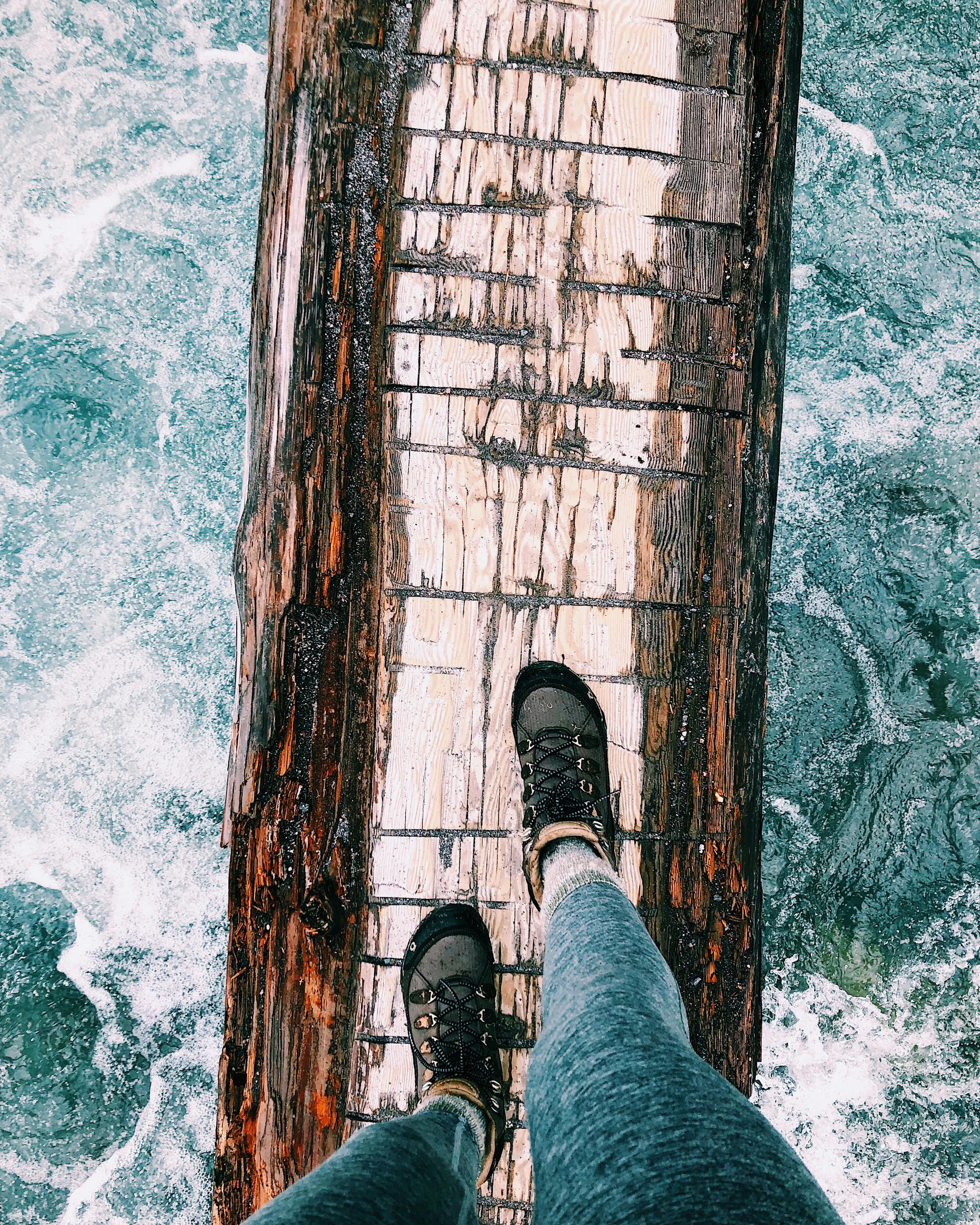 A person walks across a wooden beam suspended over the water