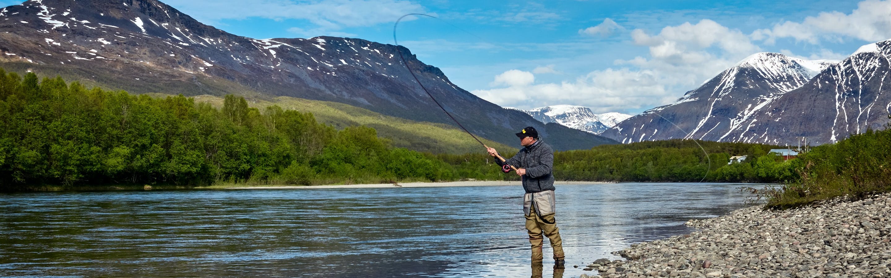 A man stands on the shore of a river and casts a fly line