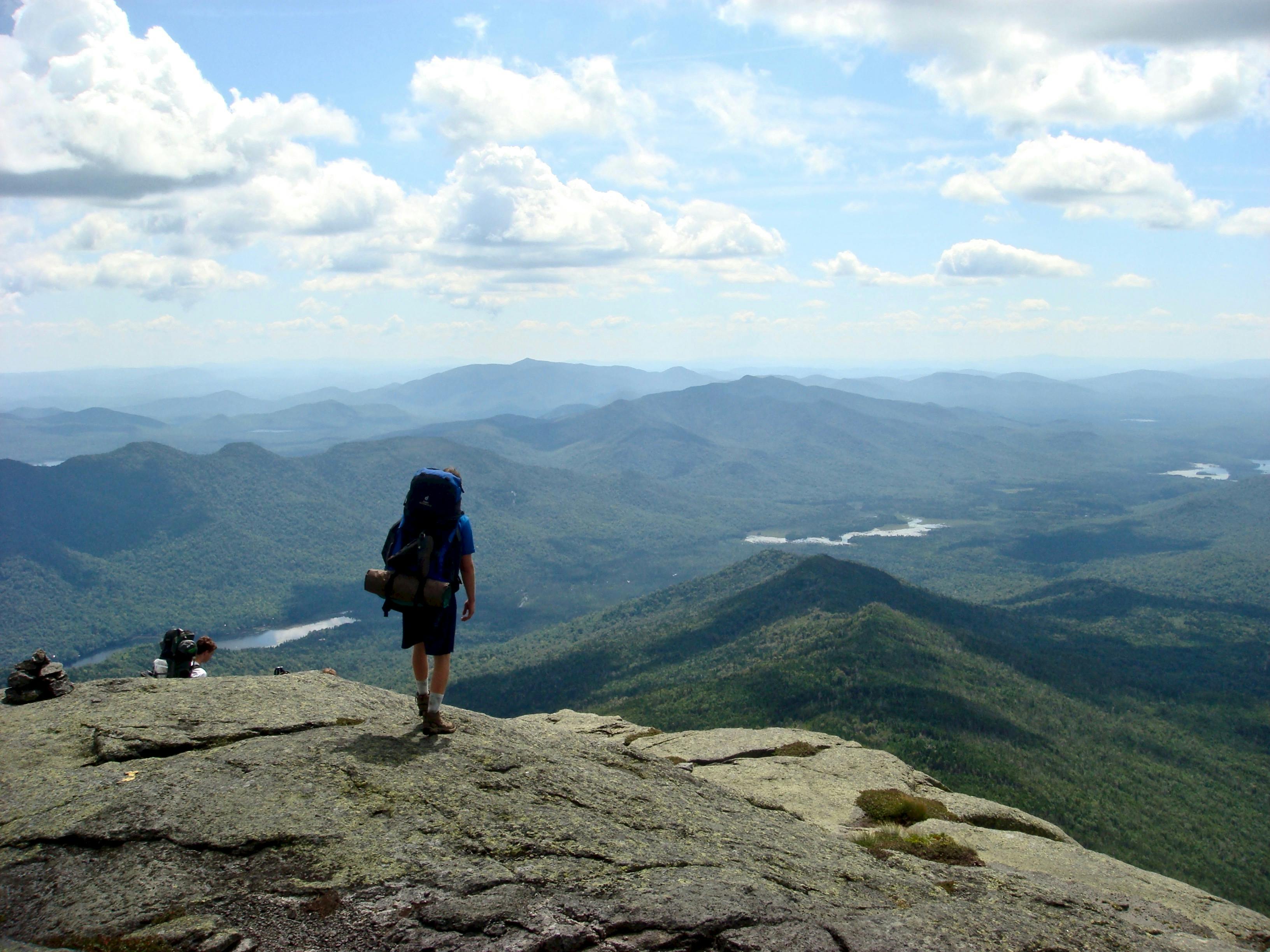 A person wearing a backpacking pack looks out at hills and mountains