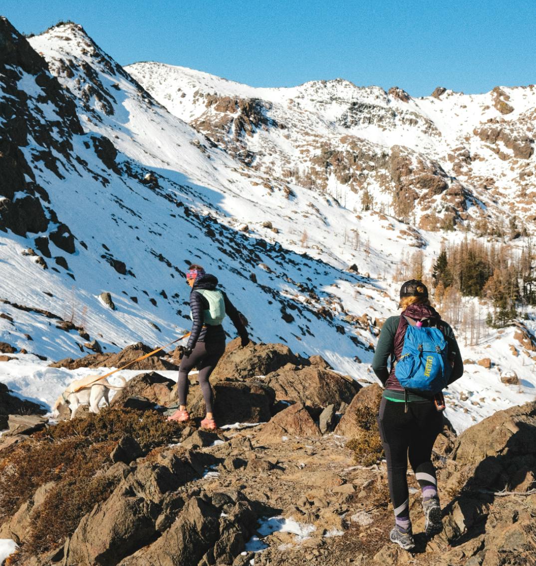 Two women with running packs navigate a snowy trail.