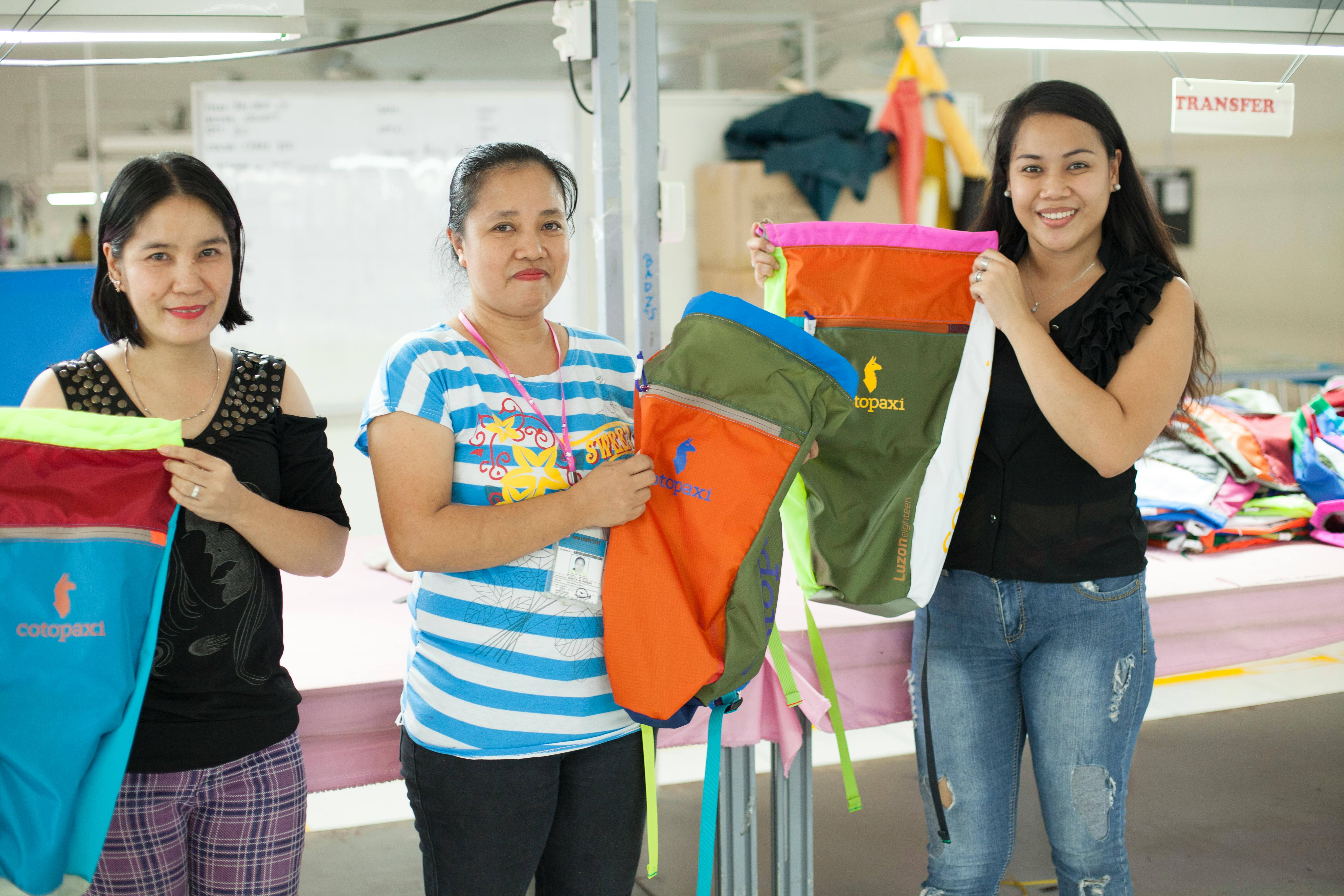 Three women holding Cotopaxi backpacks in a factory
