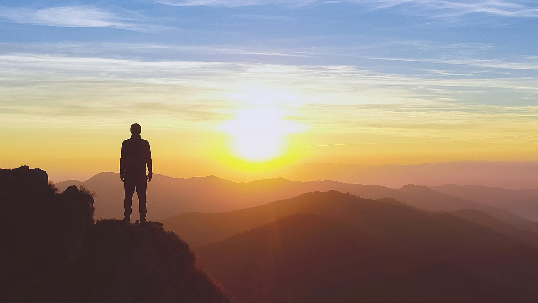 Silhouette of a man standing on a mountain with the sun rising in the background