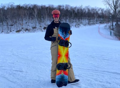 A snowboarder standing on a ski run holding the Lib Tech T.Rice Golden Orca Snowboard.