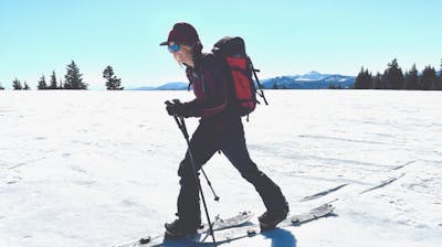A woman splitboarding in the snow. She has a backpack on and is smiling. 