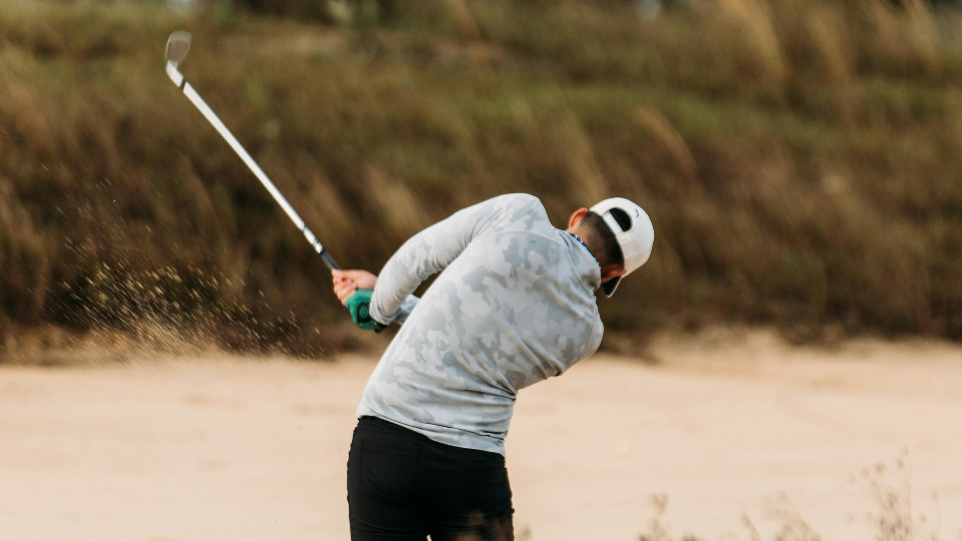 A man hits a golf ball out of the bunker. 