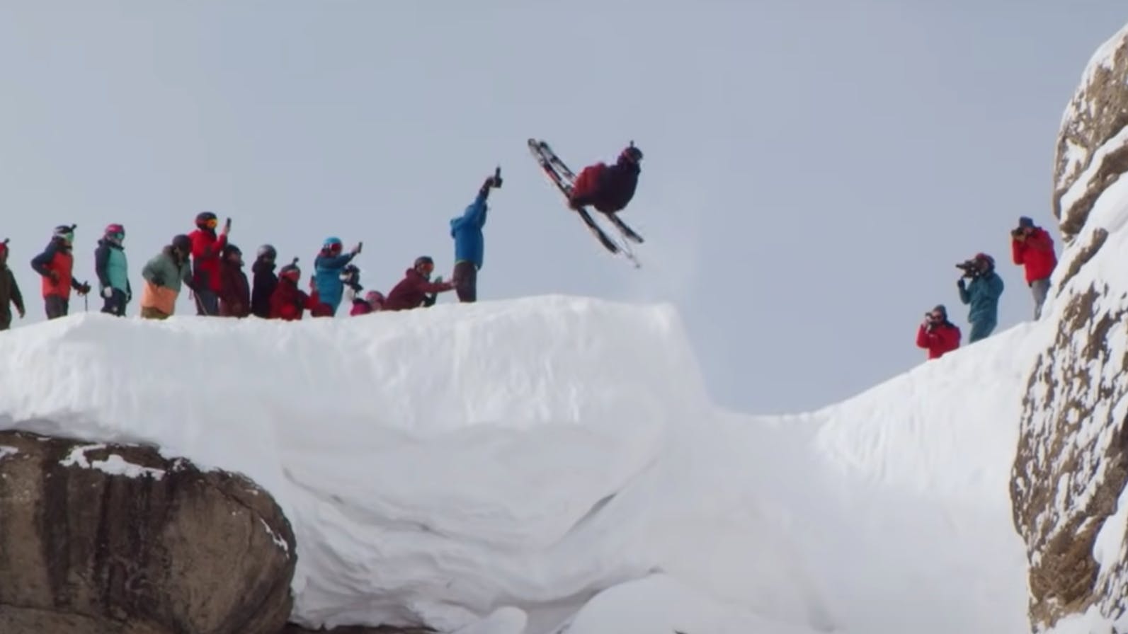 Skier jumps off the top of Corbet's couloir at Jackson Hole Mountain Resort. Many people watch as the skier does a flip. 
