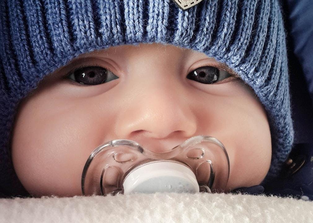 A closeup on a baby wearing a hat with a pacifier in its mouth