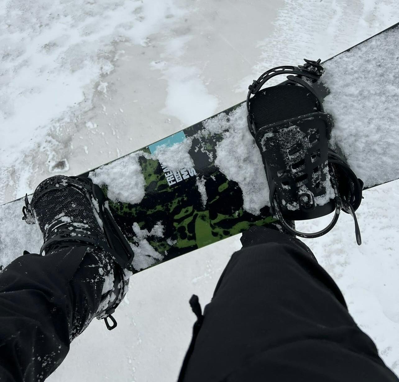 Someone takes a picture of their snowboard, boots, and bindings while on a chairlift. 