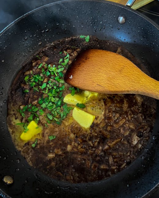 A spoon mixing up herbs and butter in a pan. 