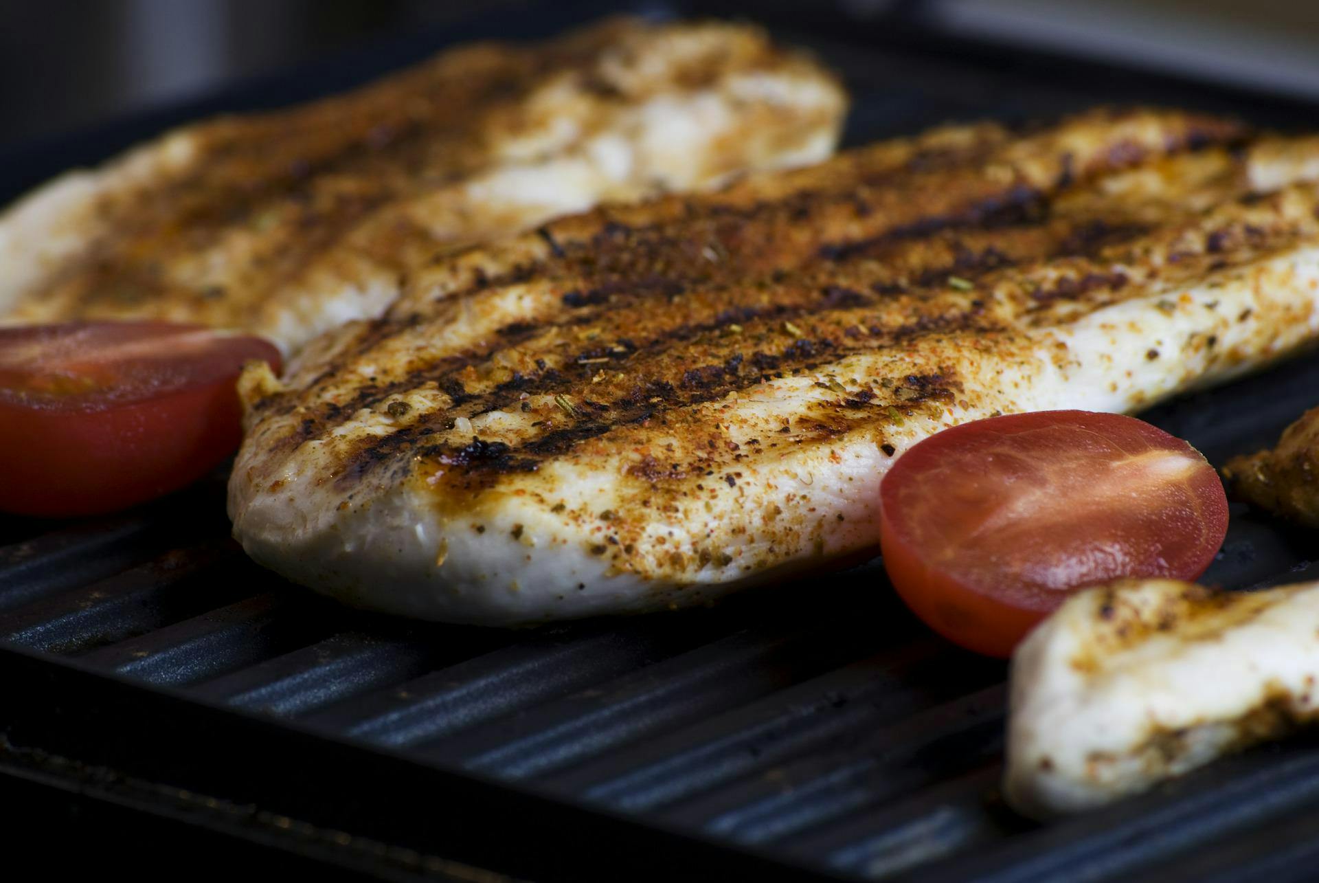 Some fish and tomatoes sit on an electric grill. 