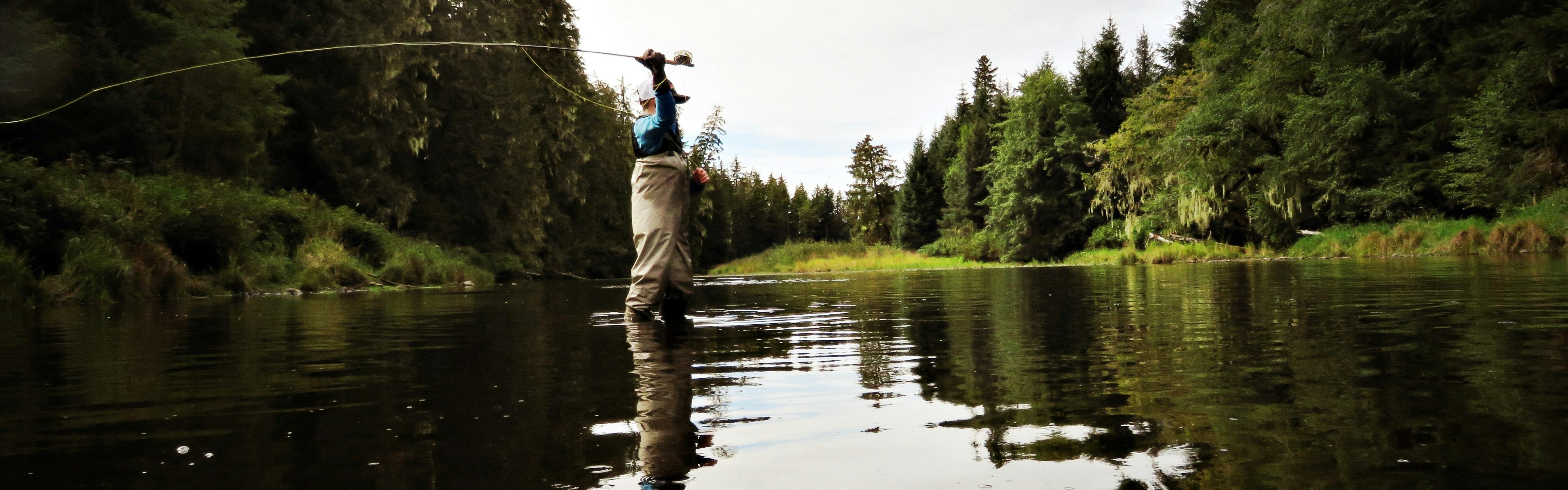 A fly fisher standing in a river casts his rod.