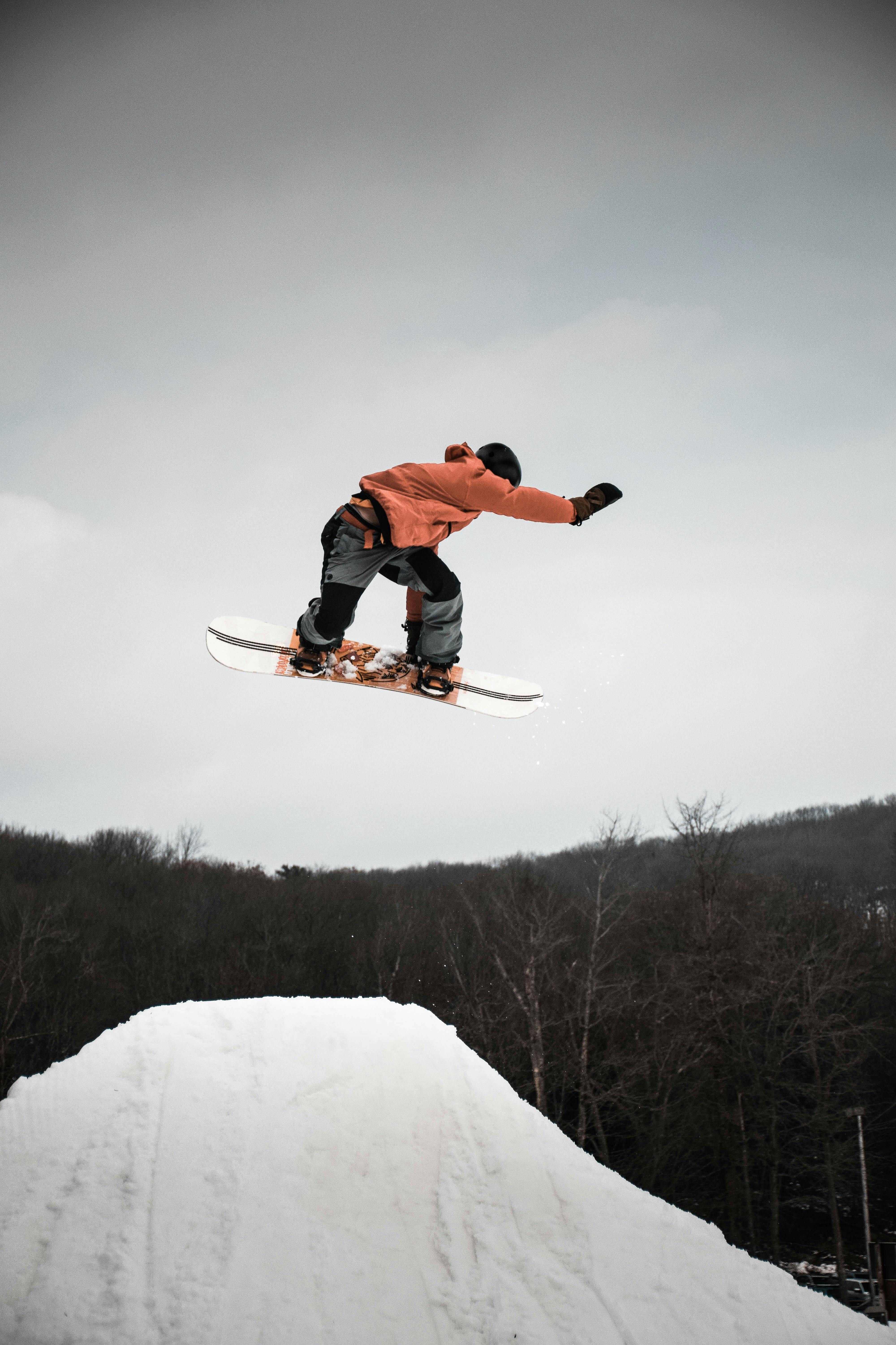 A snowboarder in an orange jacket flies through the air
