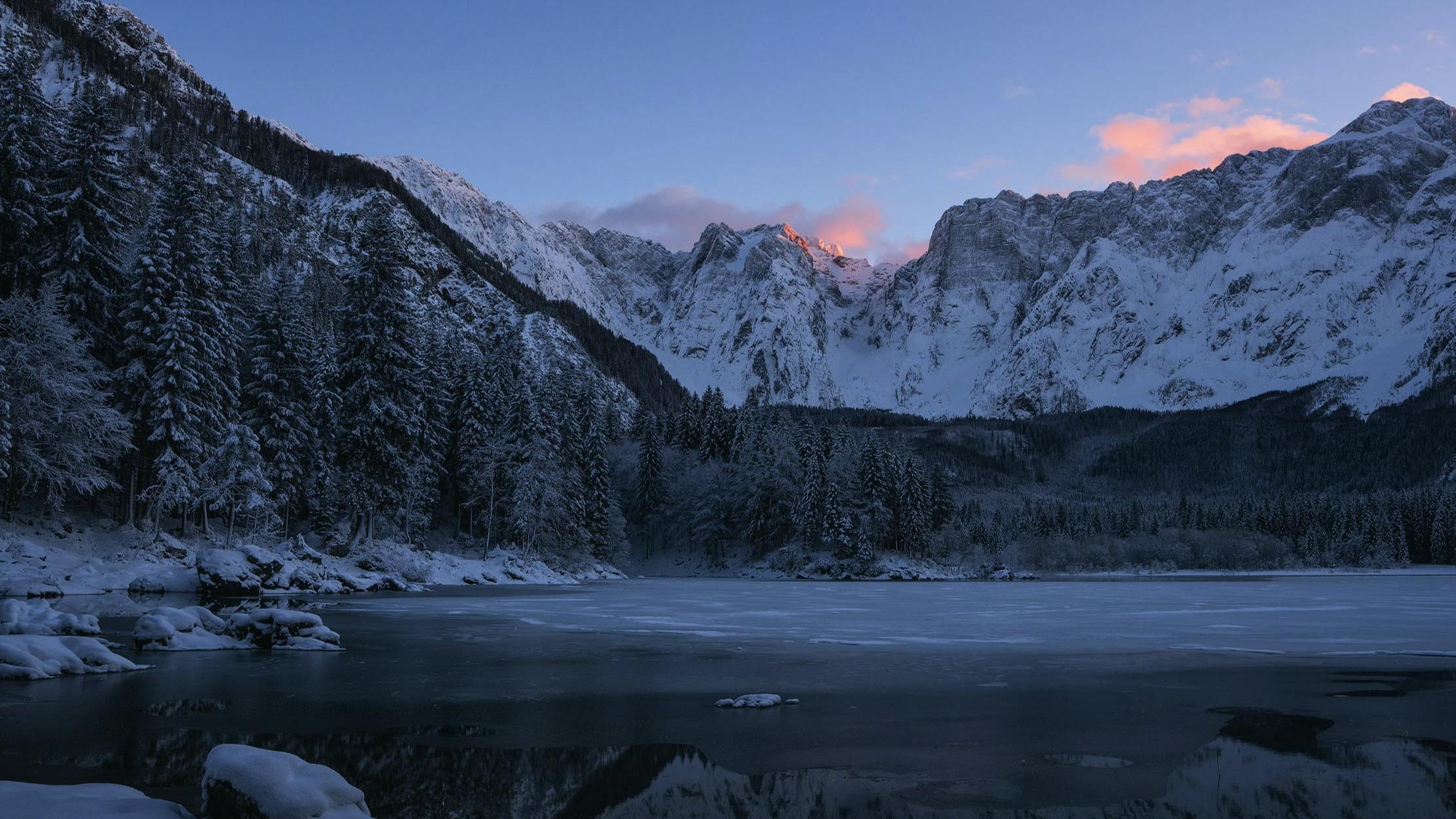A sun rises over a snowy mountain and lake. 