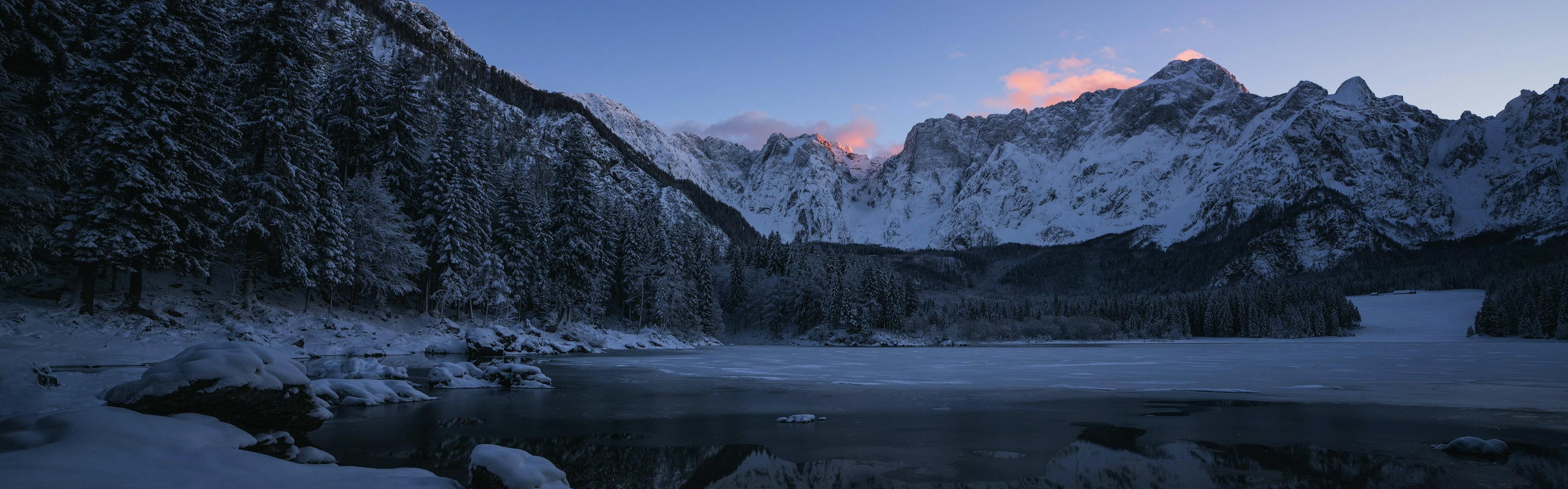 A sun rises over a snowy mountain and lake. 
