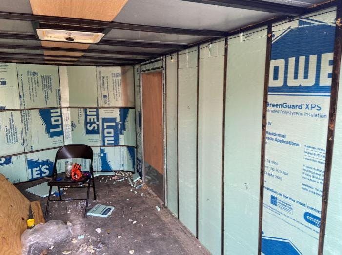 The inside of a cargo trailer that is being converted as the insulation pieces are going in. There is insulation on some of the walls and not on others.