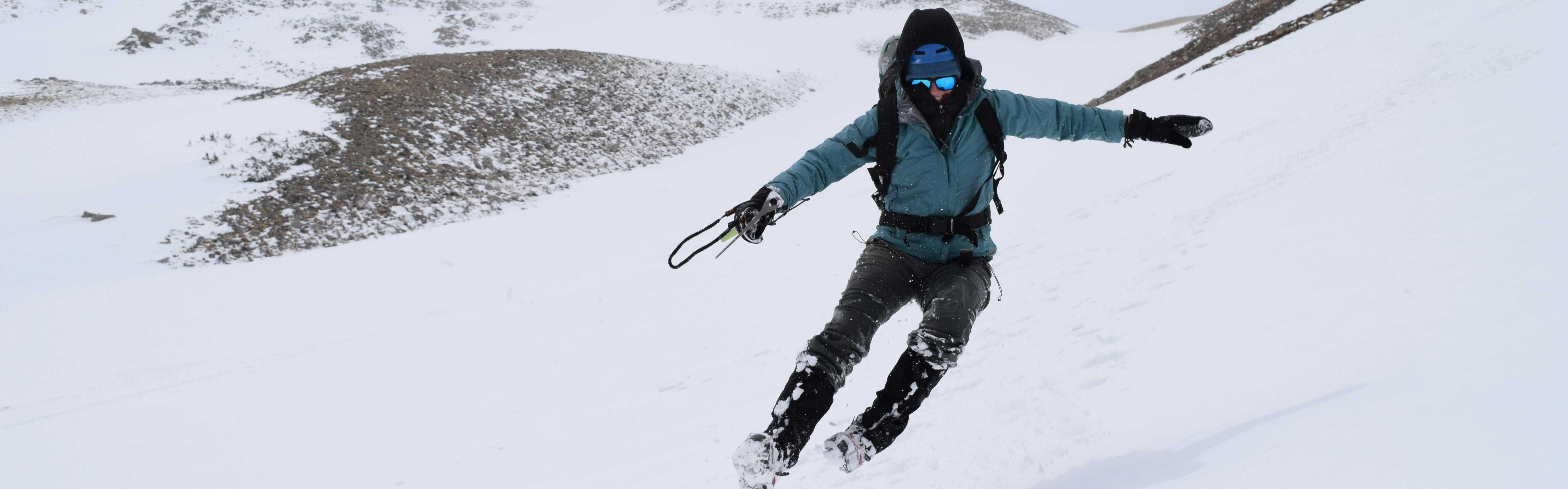 A hiker in a turquoise jacket running down a slope in the snow